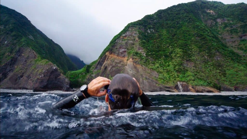 Un nageur ajuste son masque dans l’eau, face à des falaises verdoyantes, scène du film Nos âmes libres
